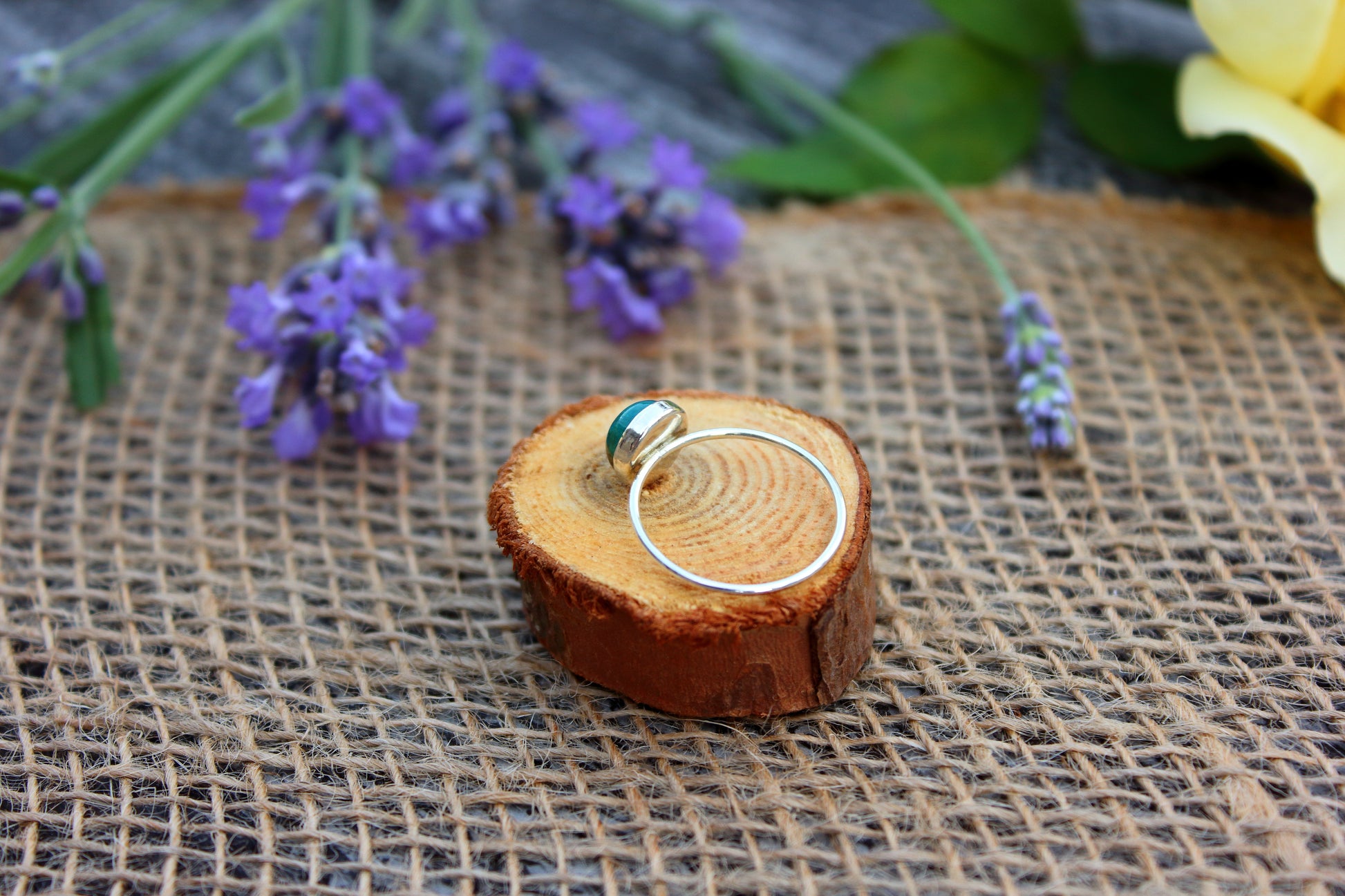 Sterling silver ring on a wooden block with purple flowers in the background