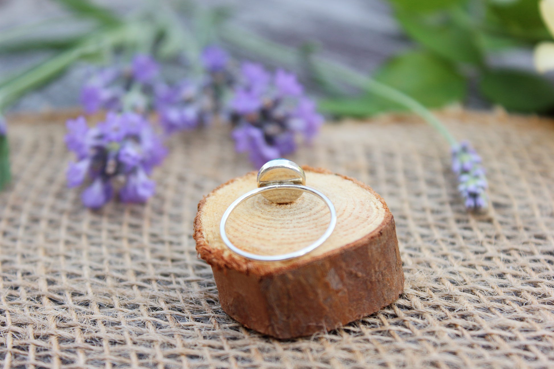 Silver ring on a wooden stand with lavender flowers in the background