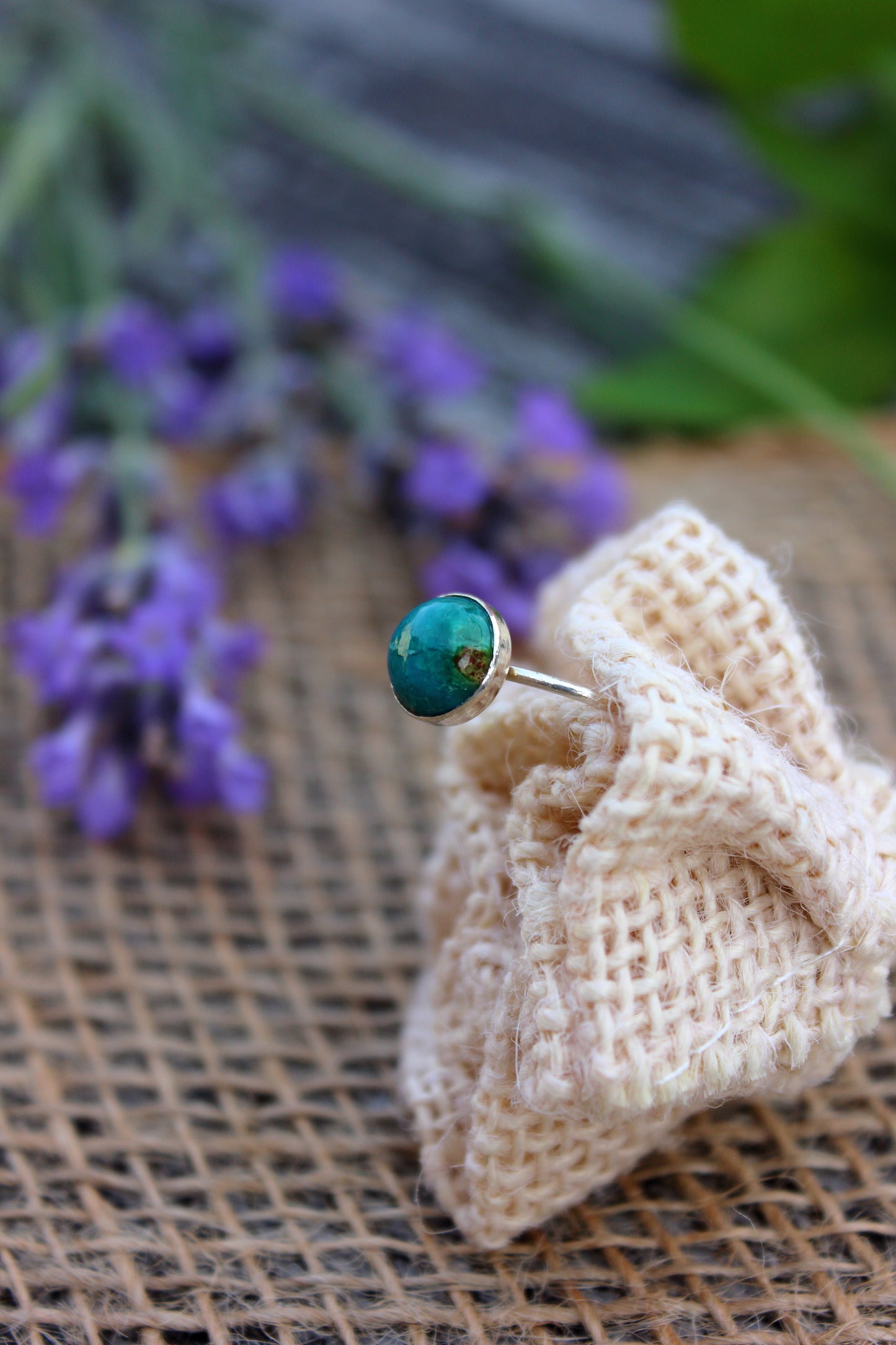 Ring with a chrysocolla stone on a beige fabric with blurred purple flowers in the background