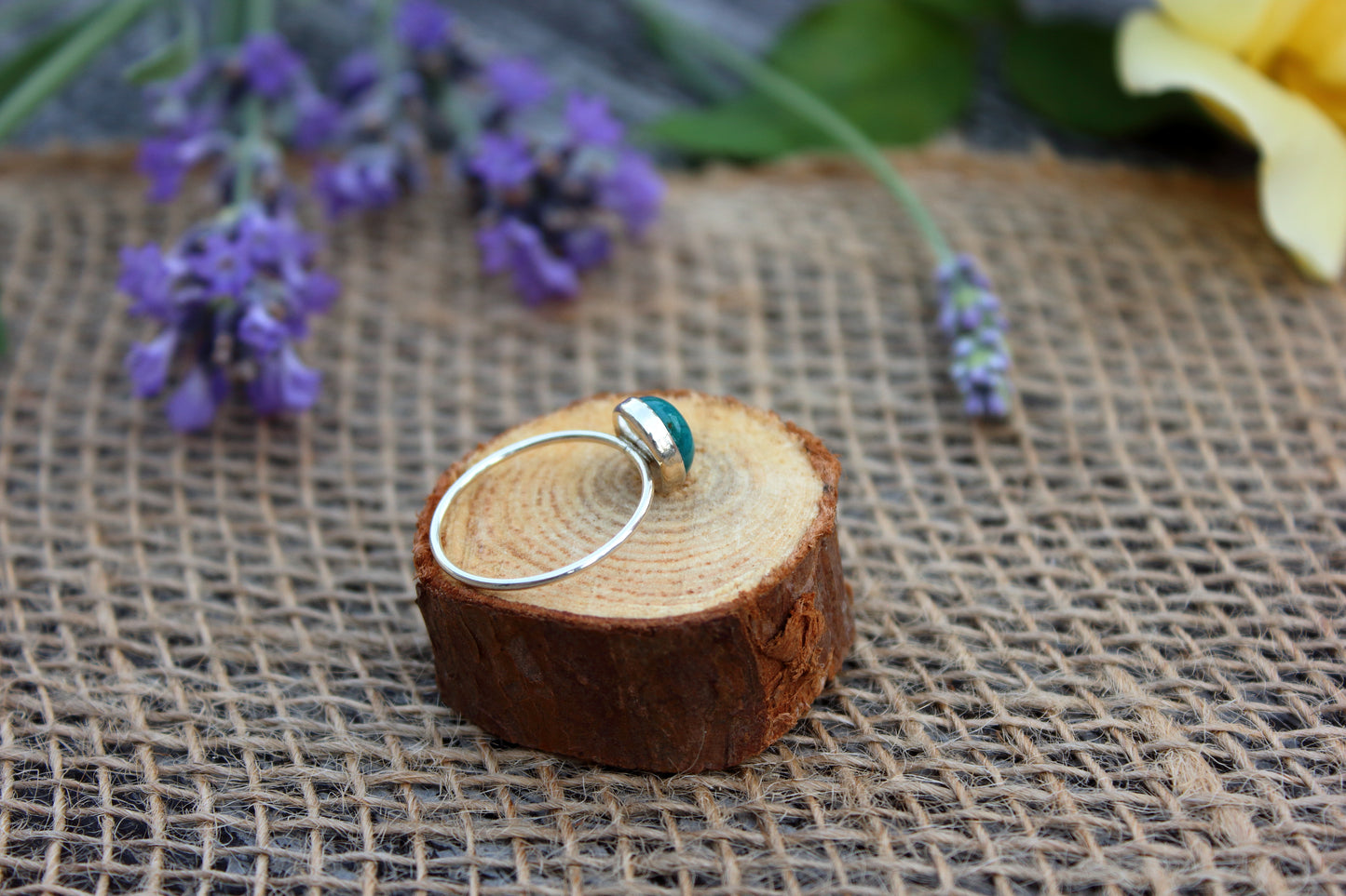 Silver ring with a blue gemstone on a wooden block with flowers in the background