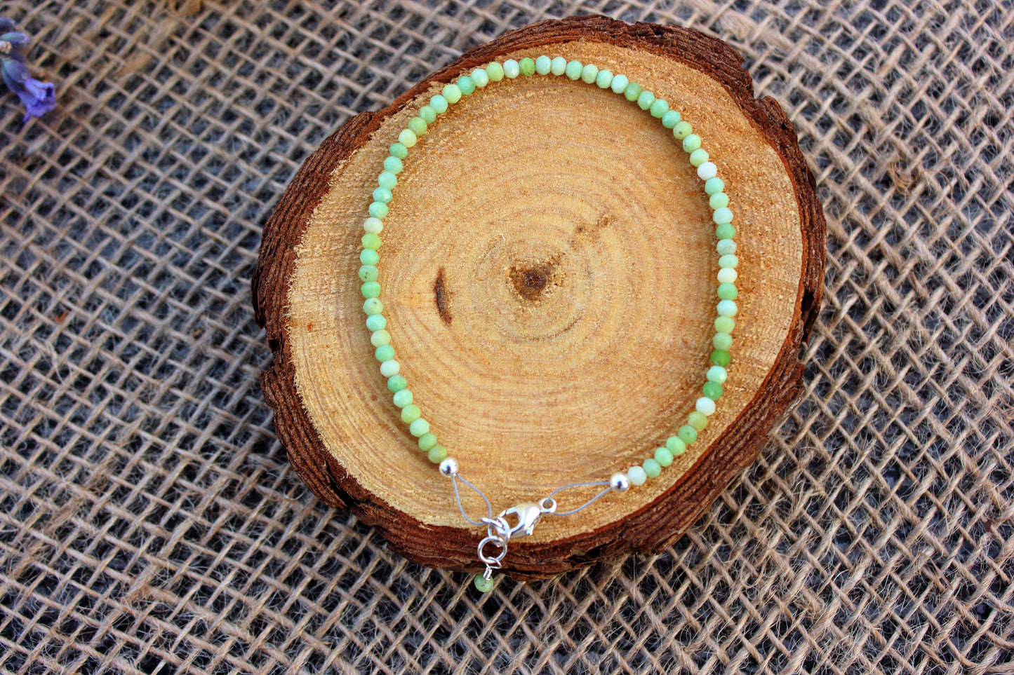 Green beaded bracelet on a wooden log with a textured fabric background