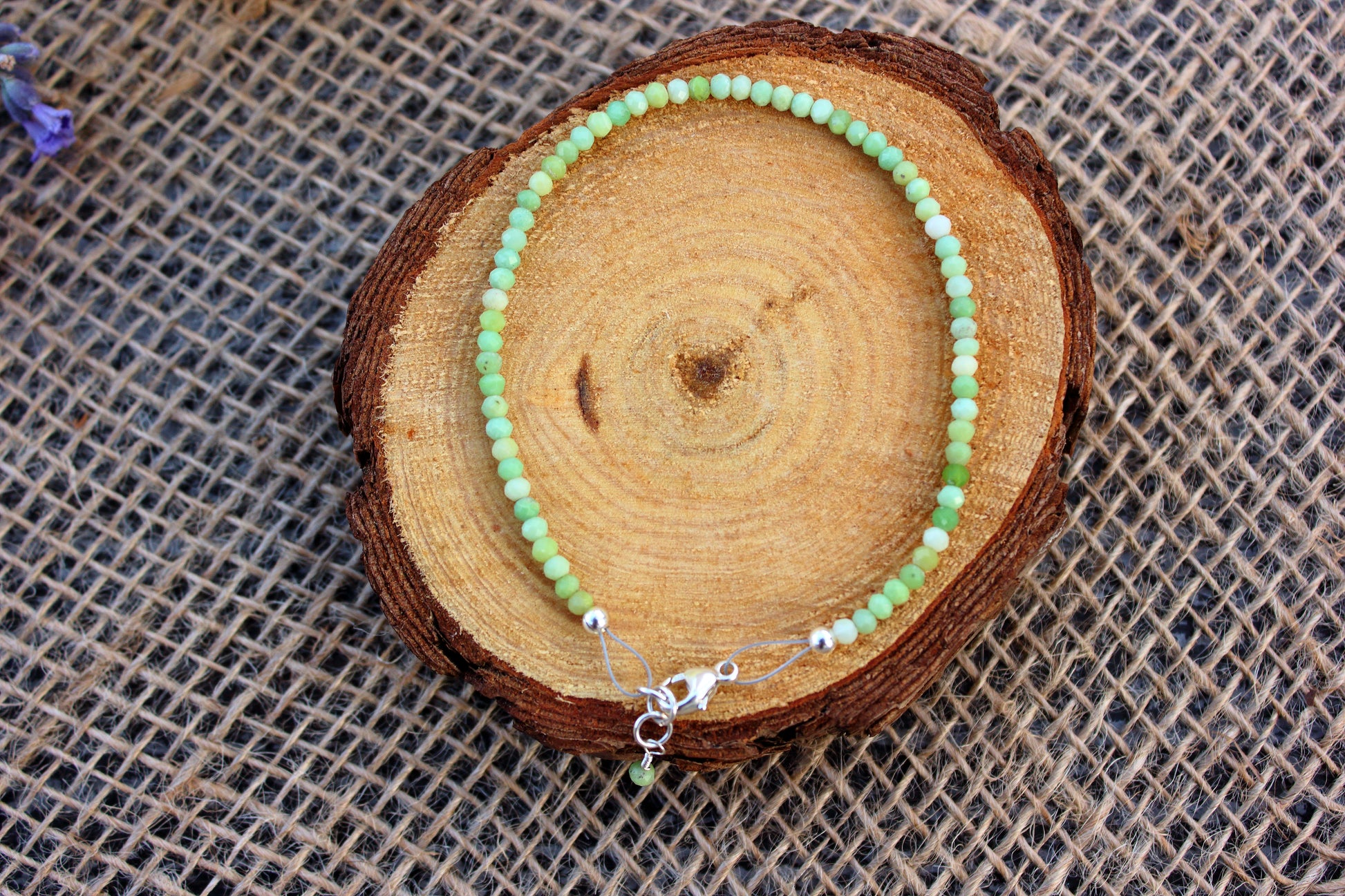 Green beaded bracelet on a wooden log with a textured fabric background