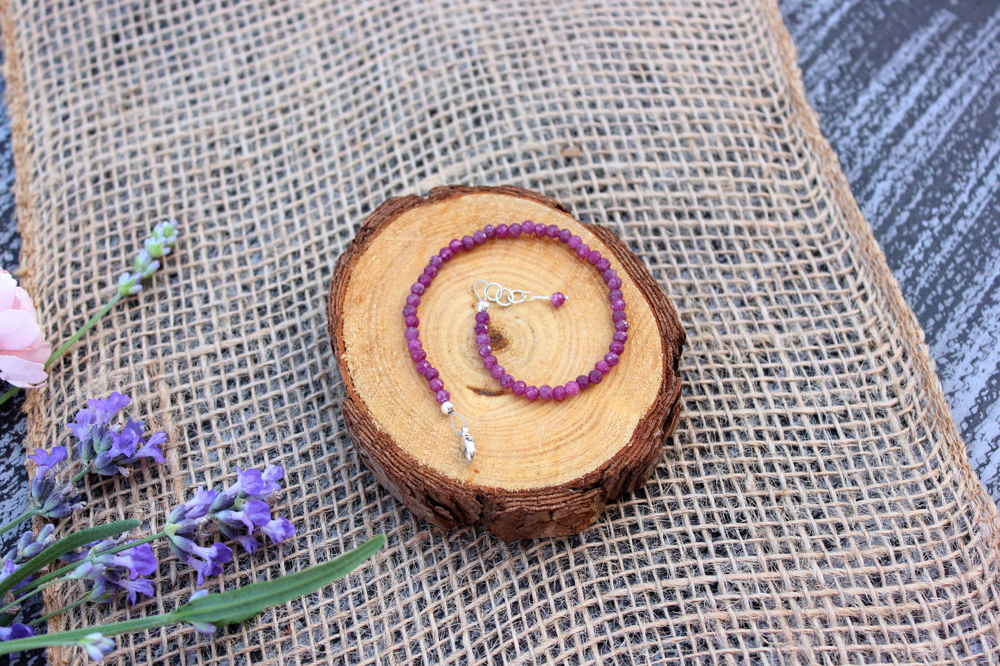 Ruby beaded bracelet on a wooden disc with lavender flowers on a textured fabric background