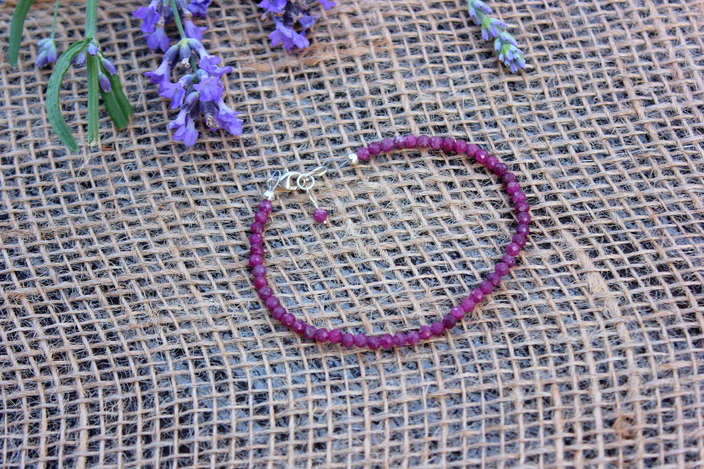 Ruby beaded bracelet on a textured fabric background with lavender flowers.